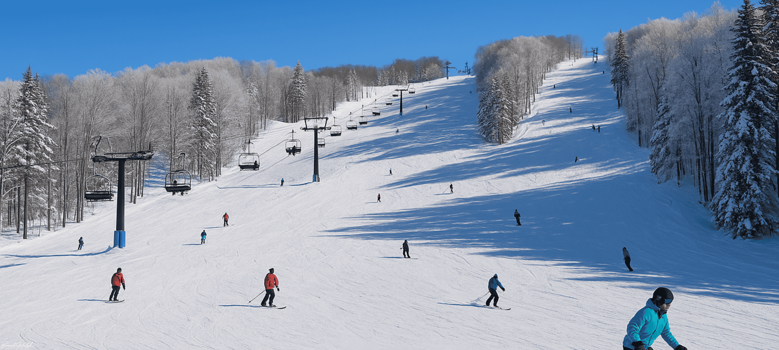 Snow-covered slopes with skiers enjoying Boyne Mountain Winter Adventure under a clear blue sky