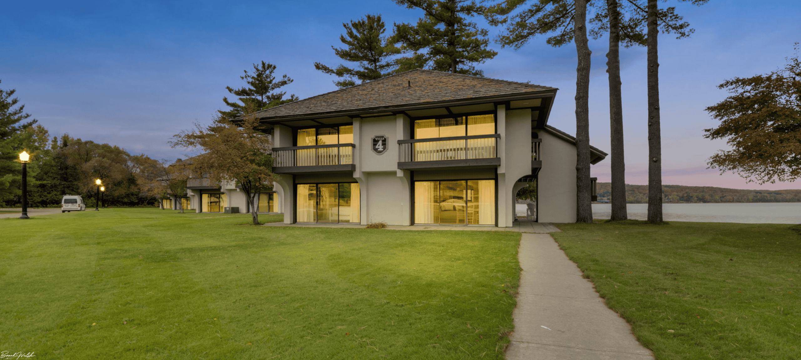 A luxurious Deer Lake villa at Boyne Mountain Resort with lakefront view and cozy outdoor seating under pine trees.